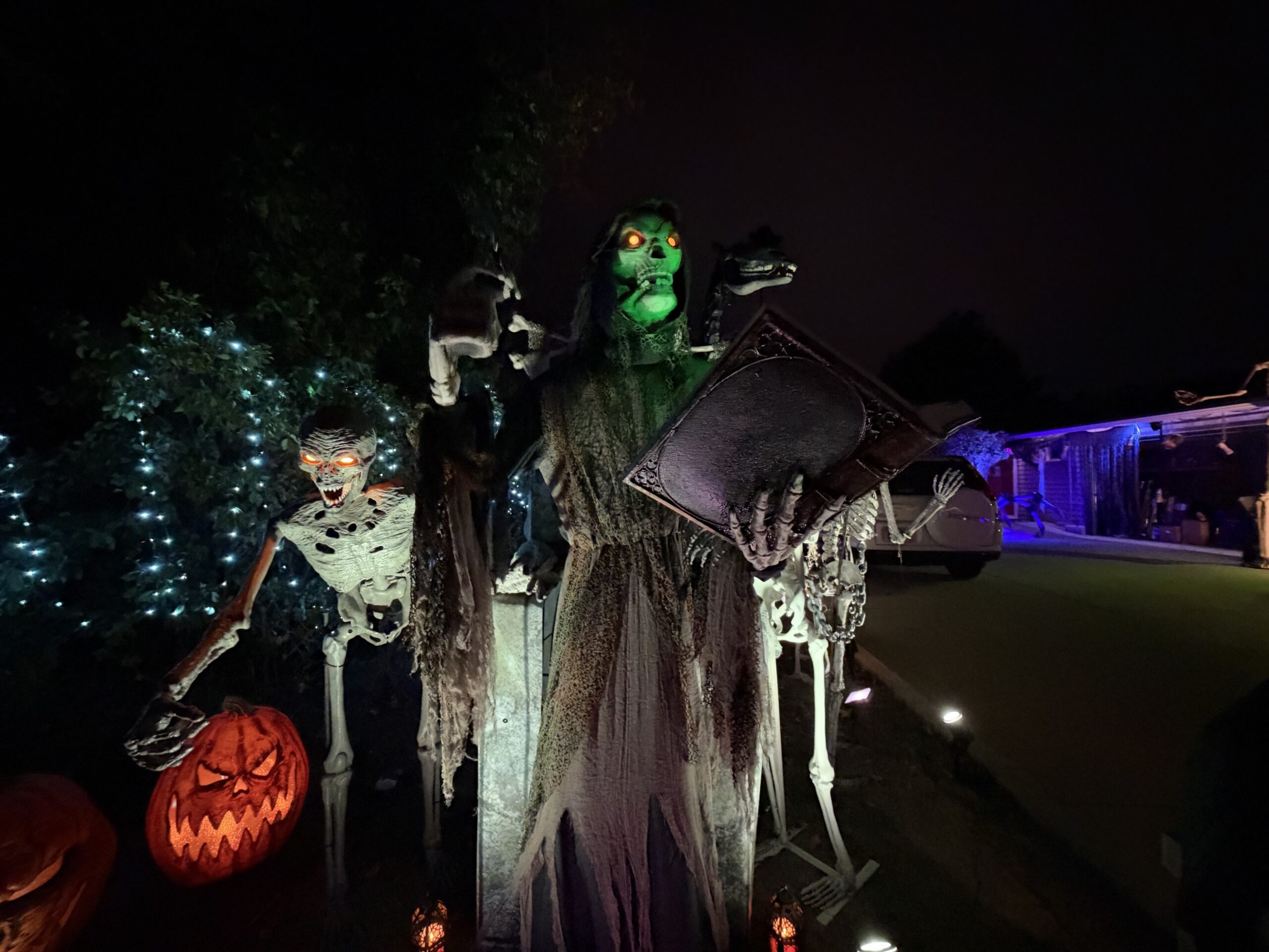 A wide view of the hooded skeletal storyteller, open book, skeletons, and glowing pumpkin.