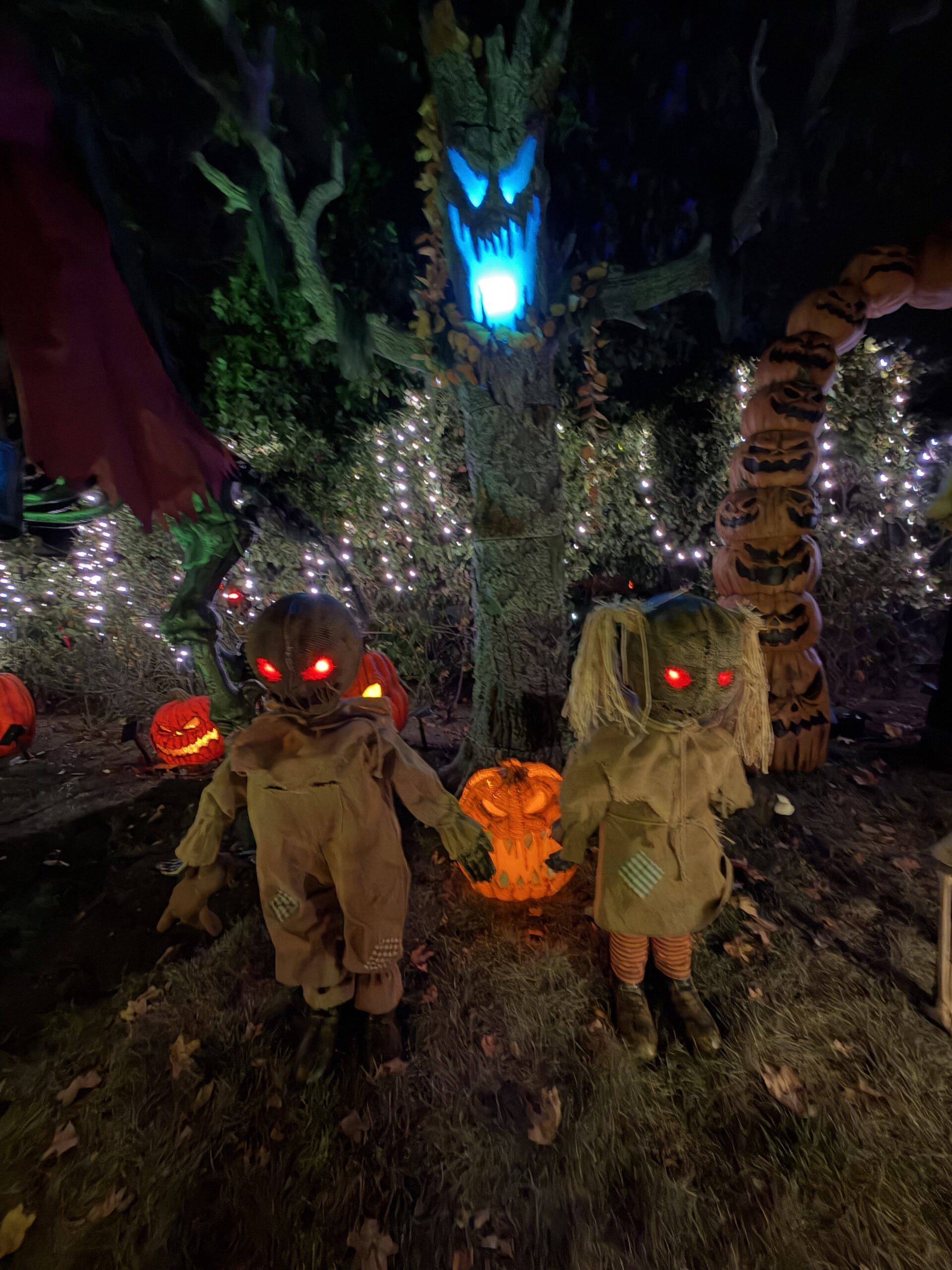 Burlap twins with red glowing eyes beneath a haunted tree and pumpkin arch.