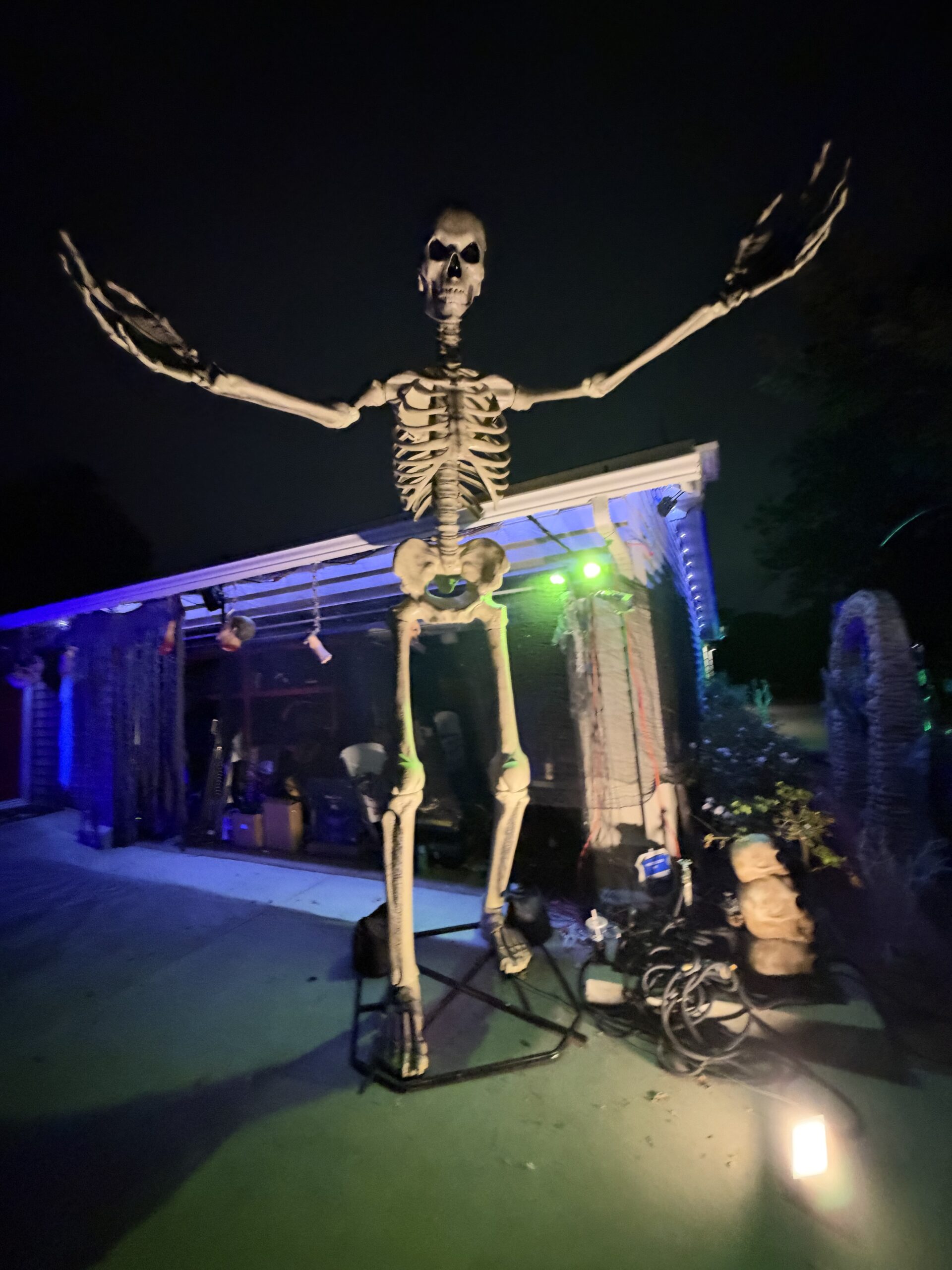 A towering skeleton with outstretched arms outside the decorated house.